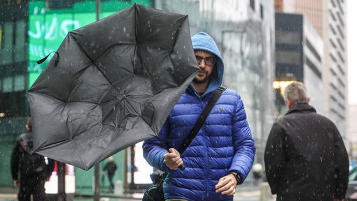 Eine Sturmböe bläst einem Mann den Regenschirm weg.