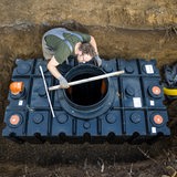 Ein Mann verbaut im Garten neben seinem Haus eine Wasserzisterne, um seinen Garten mit Regenwasser bewaessern zu koennen.