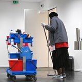 Reinigungskraft wischt einen Boden, ein Putzwagen steht neben ihr