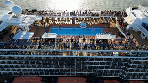 Mehrere Menschen stehen an Deck eines Kreuzfahrtschiffes