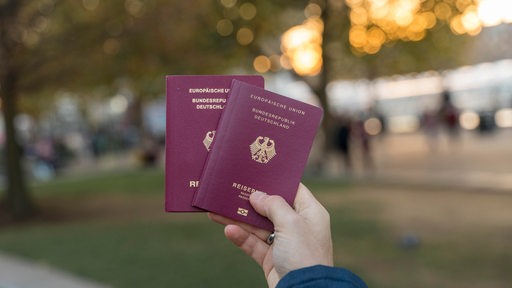Ein Mann hält zwei deutsche Reisepässe in der Hand.