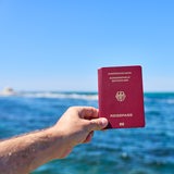 Ein Tourist hält Reisepass der Bundesrepublik Deutschland vor das Meer im Urlaub.