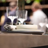 Restaurantszene: Im Vordergrund ein eingedeckter Tisch, im Hintergrund unscharf Restaurantangestellte (Symbolbild)