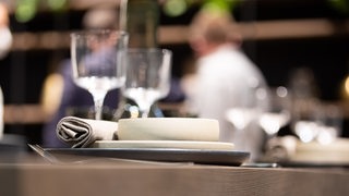 Restaurantszene: Im Vordergrund ein eingedeckter Tisch, im Hintergrund unscharf Restaurantangestellte (Symbolbild)