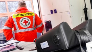 Ein Sanitäter mit einer Jacke des Deutschen Roten Kreuzes steht am Fenster eines Intensivstationszimmer in einem Krankenhaus. 
