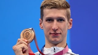 Schwimmer Florian Wellbrock hält bei der Olympia-Siegerehrung seine Bronze-Medaille hoch.