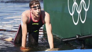Schwimmer Florian Wellbrock stützt sich erschöpft nach seinem Gold-Rennen im Freiwasser am Steg auf.