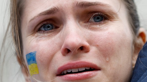 Eine weinende Frau mit ukrainischer Flagge auf der Wange