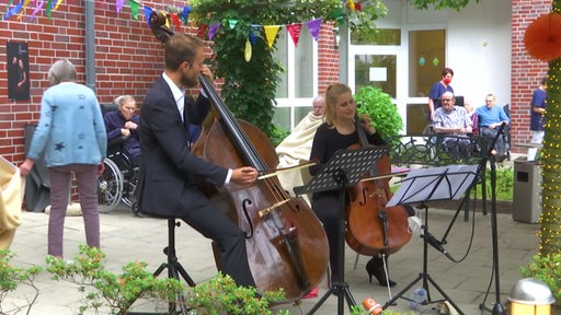 Zwei klassische Musiker machen in einem Garten eines Pflegeheims Musik für die Senioren.