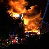 Große Flammen steigen in den Nachthimmel, davor sind Feuerwehrleute zu sehen.