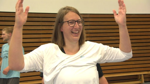 Sportblitz-Reporterin Ariane Wirth hält beide Hände in die Luft und lacht in die Kamera.