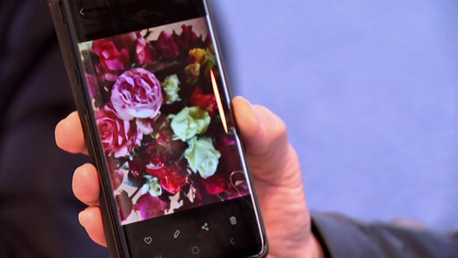Eine Hand hält ein Handy, auf dem ein Foto von einem Rosenstrauß zu sehen ist.
