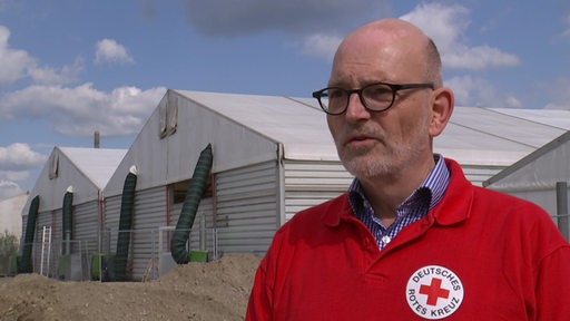 Ein Mann mit einem roten Pullover vom Deutschen Roten Kreuz steht vor der neu gebauten Zeltstadt für die Kriegsflüchtlinge aus der Ukraine.