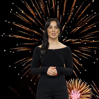 Eine Frau schaut in die Kamera - im Hintergrund ist Feuerwerk zu sehen