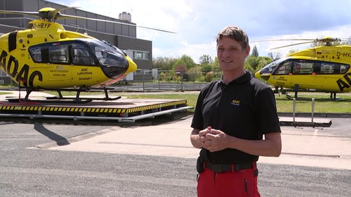 Der Rettungspilot Rüdiger Engler im Interview, im Hintergrund zwei Rettungshelikopter von ADAC.