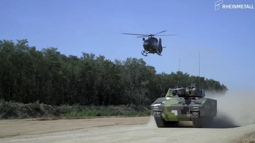 Ein Panzer und ein Hubschrauber von Rheinmetall sind in Bewegung zu sehen. 