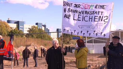 Protestanten halten Schilder hoch zum demonstrieren vor dem Russenfriedhof in Reitbrake. 