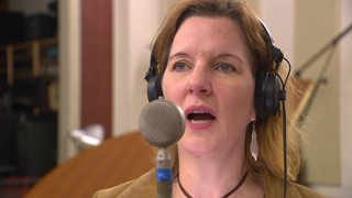 Eine Frau mit Kopfhörern singt in ein Mikrophon.