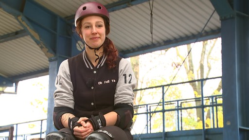 Die Rollschuh Fahrerin Sabrina Bläss sitzt mit einem Helm, Ellenbogenschoner und Knieschoner im Interview. 