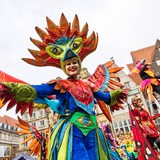 Stelzenläuferin mit bunter Maske und Flügel-Kostüm tanzt auf dem Bremer Marktplatz.