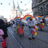 Eine Trommeltruppe in weißen Overalls. Auf ihrem Rücken sind Schwimmnudeln in unterscheidlichen Farben befestigt. Sie sollen an einen Regenbogen erinnern.