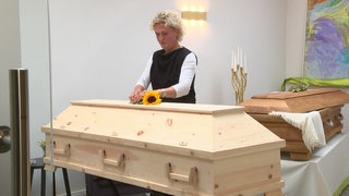 Eine Frau legt eine Sonnenblume auf einen Sarg in einem Bestattungsunternehmen.