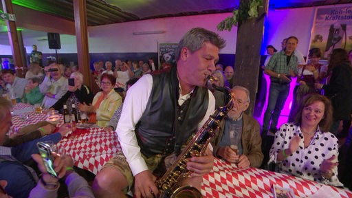 "Geri der Klostertaler" spielt Saxofon auf einer Bierbank zwischen seinem Publikum.