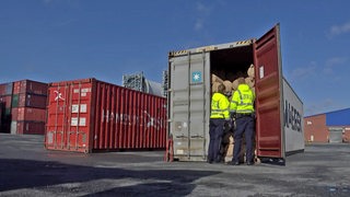 Zwei Personen in gelben Zoll-Jacken schauen in einen geöffneten Container.