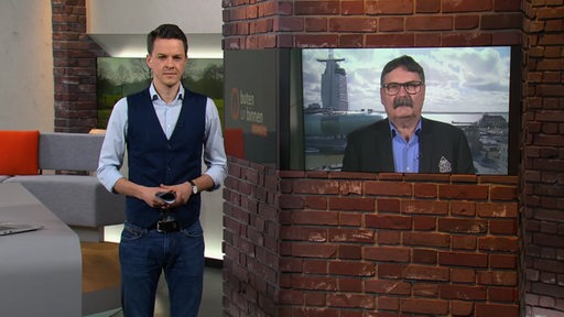 Der Moderator Janos Kereszti im Studio von buten un binnen und rechts auf dem Monitor ist der Manager von den Fischtown Pinguins zu sehen.