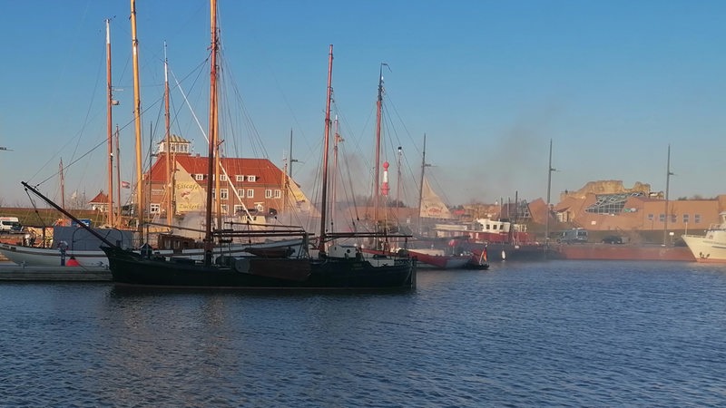 Rauch liegt über mehreren Schiffen in einem Hafenbecken.