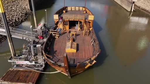 Zwei Personen stehen auf dem Koggenachbau Roland von Bremen, ein altes Holzschiff, das von vorne und oben zu sehen ist