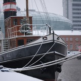 Ein Schiff liegt im Hafen. Auf dem Boot steht ein Weihnachtsbaum. Im Hintergrund das Klimahaus und das Sail City Hotel.