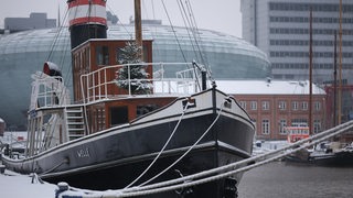Ein Schiff liegt im Hafen. Auf dem Boot steht ein Weihnachtsbaum. Im Hintergrund das Klimahaus und das Sail City Hotel.