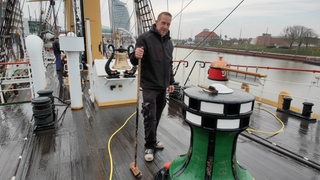 Ein Mann schrubbt das Deck eines Schiffes.