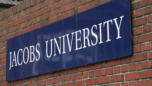 Ein blaues Schild der Jacobs Universität an einem Gebäude.