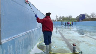 Das leere Becken des Stadionbads wird von mehreren Personen geputzt.