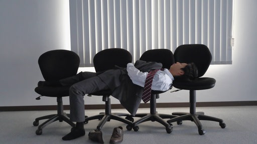 Ein Mann schläft auf mehreren Bürostühlen