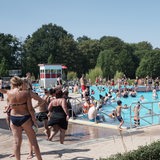 Blick auf Freibad bei Sonnenschein mit vielen Menschen im und am Wasser. 