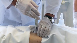 Hände mit weißen Einweghandschuhen setzen spritze an den Körper eines Patienten