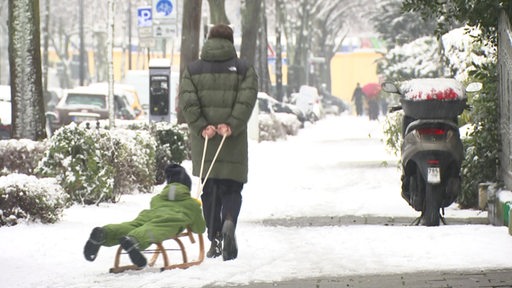 Ein Mann zieht ein Kind auf einem Schlitten durch den Schnee.
