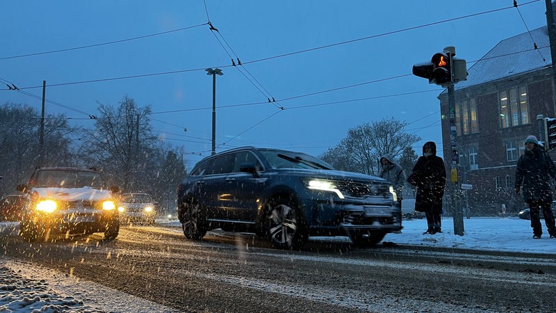 Autos fahren auf einer Straße, auf der Schnee liegt.