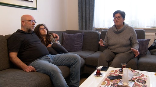 Ein Ehepaar sitzt mit ihrer Tochter auf dem Sofa.
