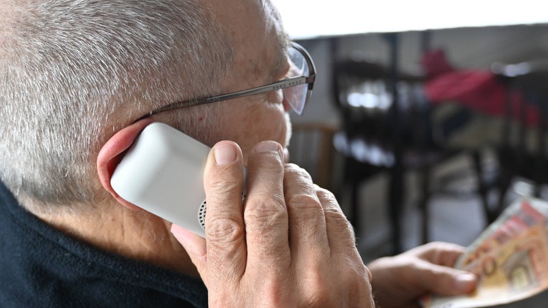 Ein Mann hält ein Telefon an seinem Ohr und Bargeld in der Hand