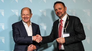 Bundeskanzler Olaf scholz und NGG-Chef Guido Zeitler reichen sich die Hand und gucken in die Kamera.