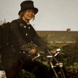 Eine Frau mit Zylinder und Schornsteinfeger-Anzug sitzt auf einem Fahrrad
