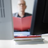 Ein Mann sitzt hinter Computerbildschirmen und liest in einem Ordner.