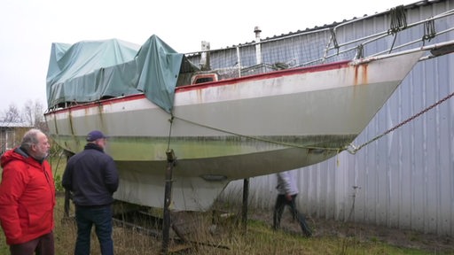 Ein Schrottboot steht auf einer Wiese an Land.