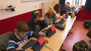 Schüler sitzen nebeneinander im Klassenzimmer und lernen am Tablet.
