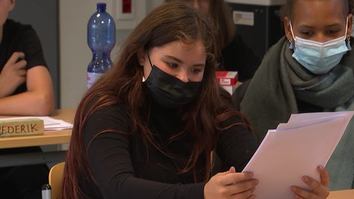 Eine Schülerin, die eine Maske trägt, schaut im Unterricht ihr Zeugnis an.