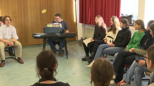 Eine Schulklasse probt gemeinsam mit dem Klassenlehrer am Keyboard ein Musical.